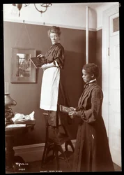 Madge Carr Cook hängt Bilder mit ihrer Magd auf, ca. 1904